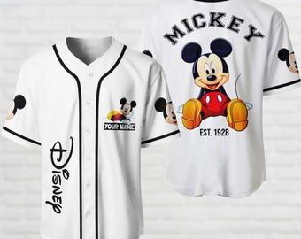 Può includere: Maglia da baseball bianca con bordini neri e un design di Topolino. La parte anteriore della maglia ha un logo Disney e il testo "YOUR NAME". La parte posteriore della maglia ha il testo "MICKEY EST. 1928" e un design di Topolino più grande.