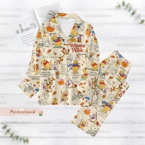 Peut inclure: Ensemble de pyjama Winnie l'ourson crème. Le haut à manches longues et le pantalon présentent un motif répété de Winnie l'ourson, Tigrou, Porcinet et Bourriquet, avec des feuilles d'automne et des citrouilles. Les mots "Winnie the Pooh" sont imprimés sur le haut.