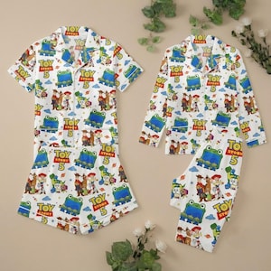 May include: Two sets of white pajamas featuring a repeating Toy Story 5 pattern with characters like Woody, Jessie, and green aliens. One set includes a short-sleeve button-down shirt and shorts, while the other features a long-sleeve button-down shirt and pants.