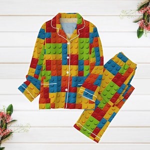 May include: A yellow, blue, red and green pyjama set with a button-up top and long trousers. The fabric features a repeating pattern of colourful building blocks.