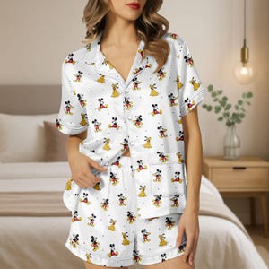 May include: White satin pajama set with a pattern of Mickey Mouse and Pluto. The short-sleeved top has a notched collar and button-down front. The shorts have an elastic waistband and a pocket. The pajamas have white trim.