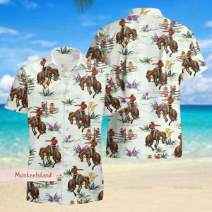 May include: A white button-up shirt with a repeating pattern of cowboys riding bucking horses. The pattern is set against a background of green grass, white fences, and purple flowers.