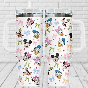 Puede incluir: Dos vasos de acero inoxidable blanco con tapas y asas. Los vasos presentan un patrón repetido de personajes de Disney, incluidos Mickey Mouse, Minnie Mouse, Donald Duck, Goofy y Daisy Duck. Los personajes están rodeados de corazones rojos y lazos de colores.