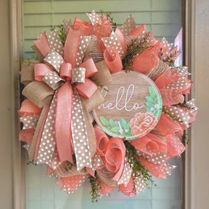 May include: A peach and brown wreath with a burlap bow and a round wooden sign that says "hello" with a floral design.