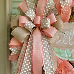 May include: A wreath with a pink and white polka dot ribbon bow. The wreath is made of burlap and has a sign that says "Hello" on it.