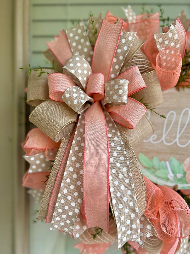 May include: A wreath with a pink and white polka dot ribbon bow. The wreath is made of burlap and has a sign that says "Hello" on it.