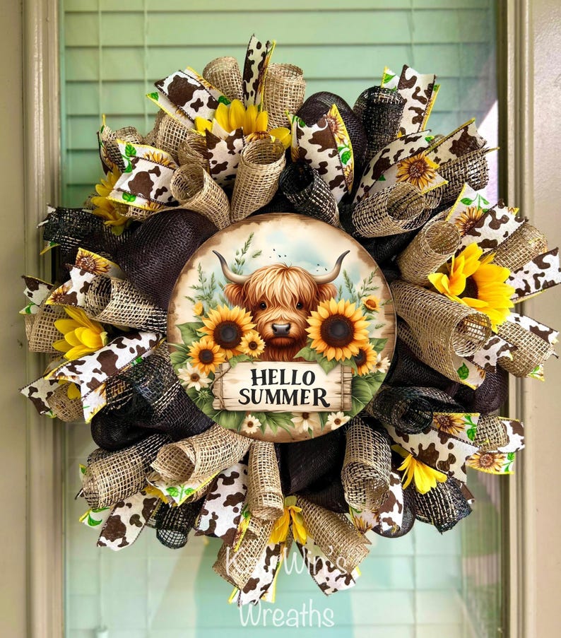 May include: A decorative wreath featuring a central circular design with a Highland cow illustration surrounded by sunflowers and the text "HELLO SUMMER." The wreath incorporates burlap, cow print, and black ribbons, along with artificial sunflowers.