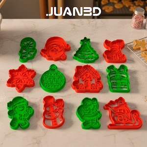 Puede incluir: Un conjunto de cortadores de galletas navideñas rojos y verdes con formas de Papá Noel, árbol de Navidad y copo de nieve. La marca "JUANED" es visible en la parte superior izquierda.