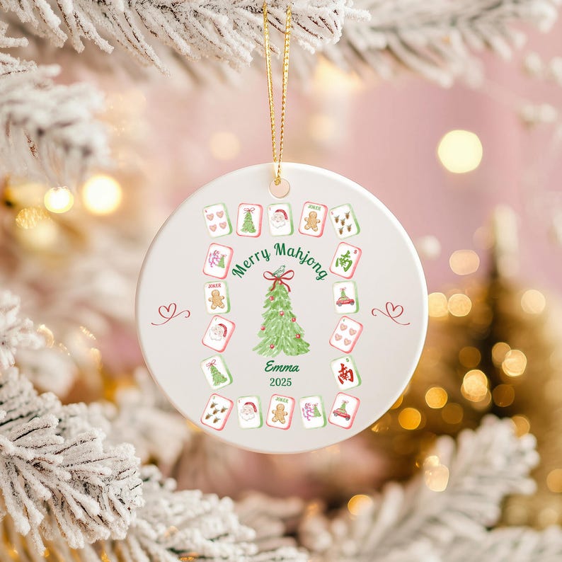 Puede incluir: Adorno navide&ntilde;o redondo y blanco con una cuerda dorada. El adorno presenta un &aacute;rbol de Navidad verde, las palabras "Merry Mahjong" y varias fichas de Mahjong. El nombre "Emma" y el a&ntilde;o "2025" tambi&eacute;n est&aacute;n impresos en el adorno.