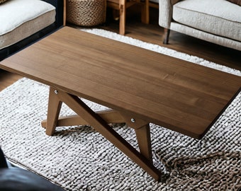 May include: A dark brown wooden coffee table with a unique X-shaped base. The table is sitting on a white fluffy rug.
