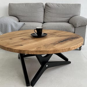 May include: A round wooden coffee table with a black metal base. The table has a natural wood finish and a unique X-shaped base.
