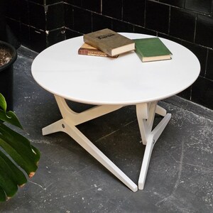 May include: White round table with a white, X-shaped base. Three books are stacked on the table, including one with the title "The Wonderful Wizard of Oz".