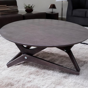May include: A dark brown round coffee table with a unique X-shaped base. The table is made of wood and has a smooth, polished finish.