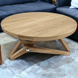 May include: A round wooden coffee table with a light brown finish and a unique X-shaped base. The table is made of solid wood and has a smooth, polished surface.