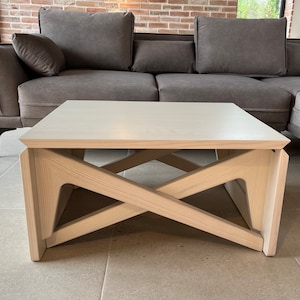 May include: A light wood coffee table with a white top and a geometric, criss-cross base.