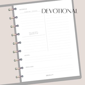 May include: A white devotional journal with a grey cover and silver binding rings. The word "DEVOTIONAL" is printed in black at the top, with sections for scripture, key takeaways, and reflection. The journal is open, revealing lined pages.