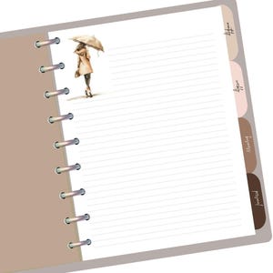 May include: A white planner with a brown cover and a spiral binding. The planner has tabs labeled "future", "weekly", "monthly", and "project". The cover features a watercolor illustration of a person walking in the rain with an umbrella.