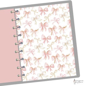 May include: A planner with a pink cover and a white page featuring a pattern of pink and gold bows. The planner is open, revealing the patterned page and the spiral binding. The design is delicate and feminine.