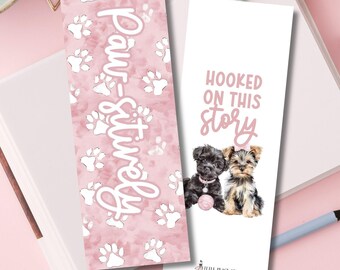 May include: Two decorative bookmarks. One pink bookmark features white paw prints and the text "Paw-sitively". The other white bookmark has the text "Hooked on this Story" and illustrations of two puppies.