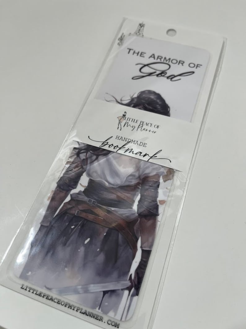 May include: A white bookmark with a watercolor illustration of a woman wearing armor. The text "THE ARMOR OF GOD" is at the top of the bookmark. The text "LITTLE PEACE OF MY PLANNER" and "HANDMADE BOOKMARK" are at the bottom of the bookmark.