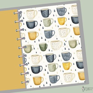 May include: A planner insert featuring a pattern of watercolor mugs in various colors, including blue, yellow, and green, with a cream background and black raindrop accents. The planner insert has a yellow cover and silver binding rings.