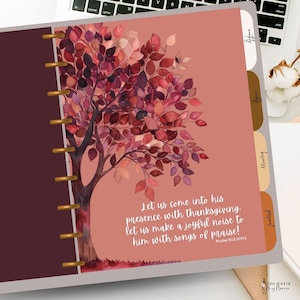 May include: A pink and brown planner with a watercolor painting of a tree with red, orange, and purple leaves. The text "Let us come into his presence with thanksgiving. Let us make a joyful noise to him with songs of praise! Psalm 95:2 (ESV)" is printed on the planner.