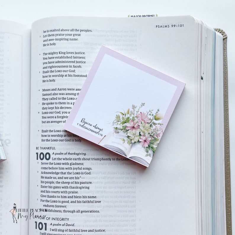 May include: A pink and white floral bookmark with the text "Rejoice always 1 Thessalonians 5:16" on a white background. The bookmark is placed on an open Bible with the text "PSALMS 99-101" visible.