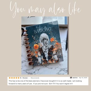 Puede incluir: Un planificador con espiral con una cubierta que presenta a una mujer con cabello largo y plateado y las palabras "She is Strong". El dise&ntilde;o de la cubierta incluye rosas naranjas y una espada. El planificador tiene una encuadernaci&oacute;n de color cobre.