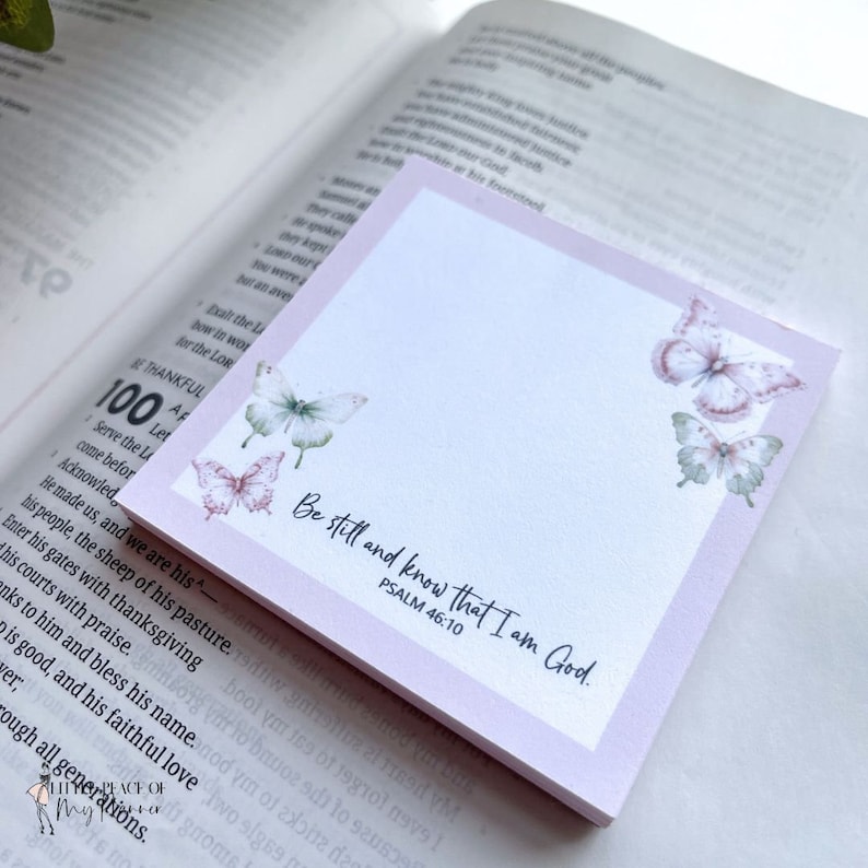 May include: A pink and white notepad with a quote from Psalm 46:10, "Be still and know that I am God." The notepad has a watercolor butterfly design.