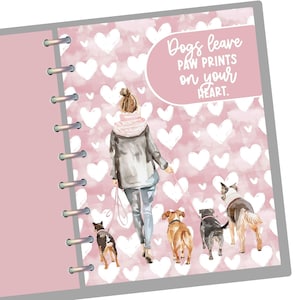 May include: A pink planner with a watercolor illustration of a person walking five dogs. The background features white hearts on a pink backdrop. The text "Dogs leave paw prints on your heart" is displayed in a white script.