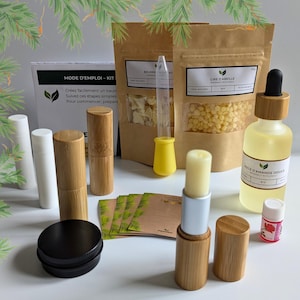 Peut inclure: Un kit de fabrication de baume à lèvres avec des ingrédients naturels, notamment de la cire d'abeille, du beurre de karité et de l'huile d'amande douce. Le kit comprend quatre tubes de baume à lèvres vides, une petite boîte et des instructions en français. Le kit est disposé sur une surface en bois avec des branches de pin en arrière-plan.