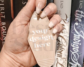 May include: A beige motel key tag with the text "your design here" in white. The key tag is being held by a hand with long, white nails.