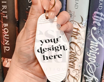 May include: White motel key chain with a gold ring. The keychain has black text that says "your design here" and "BOUTIQU".