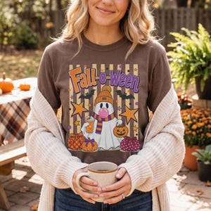 May include: A brown t-shirt featuring a graphic of a ghost wearing a beanie and scarf, holding a drink and a pumpkin bucket. The design includes the text Fall-o-ween, stars, bats, and various pumpkins against a background of vertical stripes.