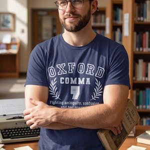 Puede incluir: Una camiseta de manga corta en color azul marino con el texto OXFORD COMMA impreso en blanco, un gráfico de una coma con ramas de laurel y el texto Fighting ambiguity, confusion and bad grammar debajo del diseño principal.