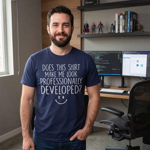 Könnte beinhalten: Ein marineblaues Kurzarm-T-Shirt mit weißem Text, der "DOES THIS SHIRT MAKE ME LOOK PROFESSIONALLY DEVELOPED?" lautet, über einer einfachen, weiß gezeichneten Smiley-Grafik, die mittig auf der Brust des Kleidungsstücks platziert ist.