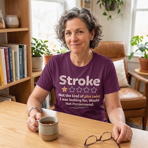 Peut inclure: Un t-shirt à manches courtes violet foncé avec le texte blanc "Stroke" au-dessus d'une étoile jaune et quatre contours d'étoiles vides. En dessous, le texte indique "Not the kind of plot twist I was looking for, Would Not Recommend."