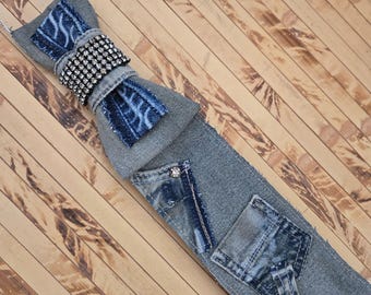 May include: A necktie crafted from gray denim fabric featuring a bow tie accent at the top. The bow tie is embellished with a band of clear rhinestones and blue patterned denim patches. The main body includes two small denim pockets and a silver stud.