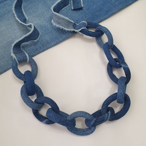 May include: A blue denim chain necklace made from strips of denim fabric sewn together. The chain is made of large, oval-shaped links.