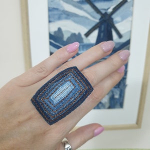 Peut inclure: Une bague en jean avec un design en couches. La bague est faite de plusieurs morceaux de jean cousus ensemble pour créer une forme géométrique.