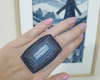 Puede incluir: Un anillo de mezclilla con un diseño en capas. El anillo está hecho de varias piezas de mezclilla cosidas juntas para crear una forma geométrica.