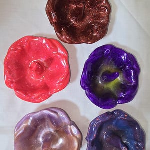 May include: Five resin ring dishes in various colors, including red, purple, brown, and two shades of purple. Each dish has a raised center and a slightly ruffled edge.