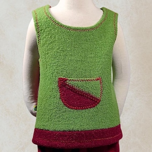 Könnte beinhalten: Ein grünes ärmelloses Oberteil und eine rote Hose für ein Kleinkind. Das Oberteil hat eine rote Tasche und einen roten Besatz. Die Hose ist rot mit dunkelblauen und grünen Bündchen. Das Outfit wird auf einer Schaufensterpuppe präsentiert.