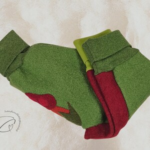 Pode incluir: Meia de Natal de feltro verde e vermelho com punho dobrado. A meia tem um design de aplica&ccedil;&atilde;o vermelho e &eacute; feita de um material macio e texturizado. O fundo &eacute; de cor clara e neutra.