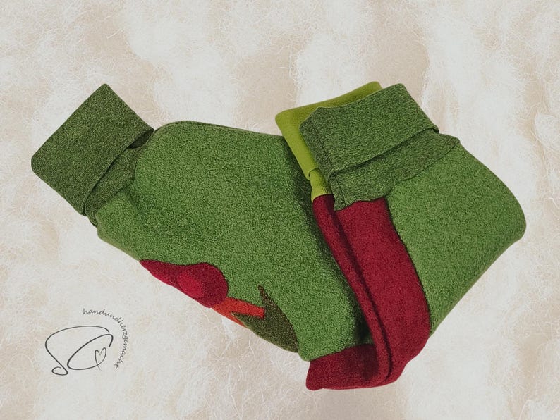 Pode incluir: Meia de Natal de feltro verde e vermelho com punho dobrado. A meia tem um design de aplica&ccedil;&atilde;o vermelho e &eacute; feita de um material macio e texturizado. O fundo &eacute; de cor clara e neutra.