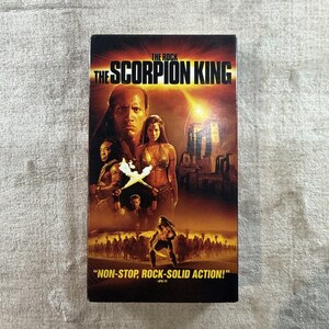 May include: A VHS tape for the movie "The Scorpion King" starring The Rock. The cover features a movie poster with images of the actors and the text "NON-STOP, ROCK-SOLID ACTION!"