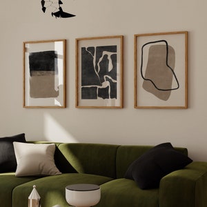 May include: Three framed abstract art prints with black and brown geometric shapes on a white background. The prints are hanging on a wall above a green sofa.