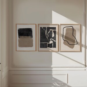 May include: Three abstract art prints in black and beige frames. The prints feature abstract shapes and lines in black and beige.
