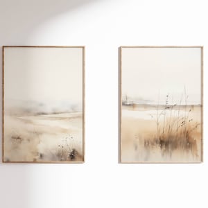 以下が含まれることがあります： 高い草と霞んだ背景を持つ風景を描いた、額縁付きの水彩画2点。絵画は茶色、ベージュ、白のトーンで描かれている。