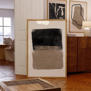 May include: Three framed abstract art prints with black and brown shapes on a white background. The prints are hanging on a white wall above a wooden dresser.